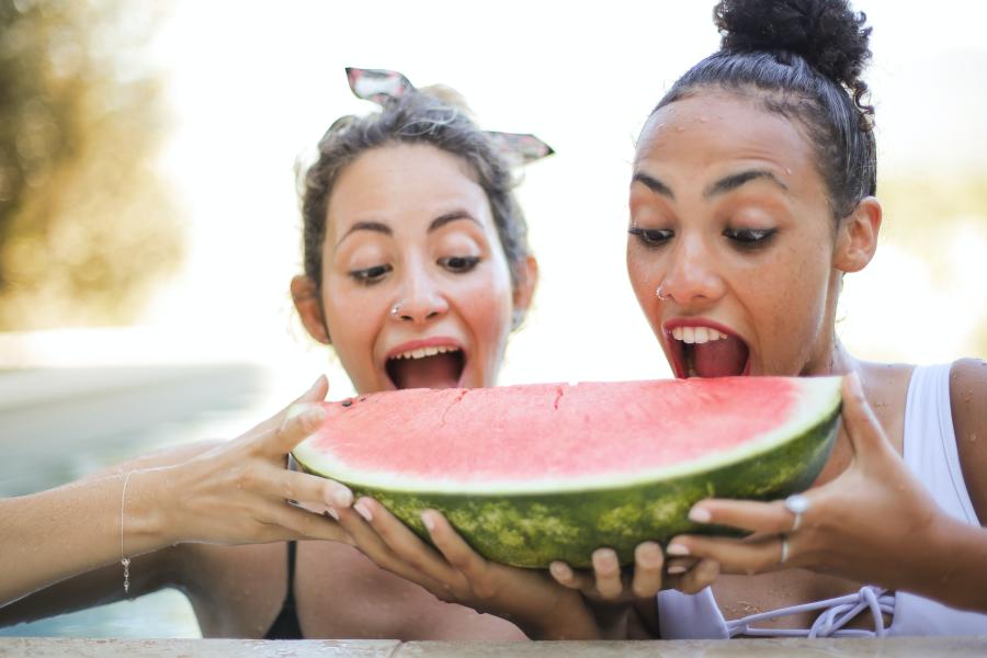 Two women about to bite into a large slice of watermelon