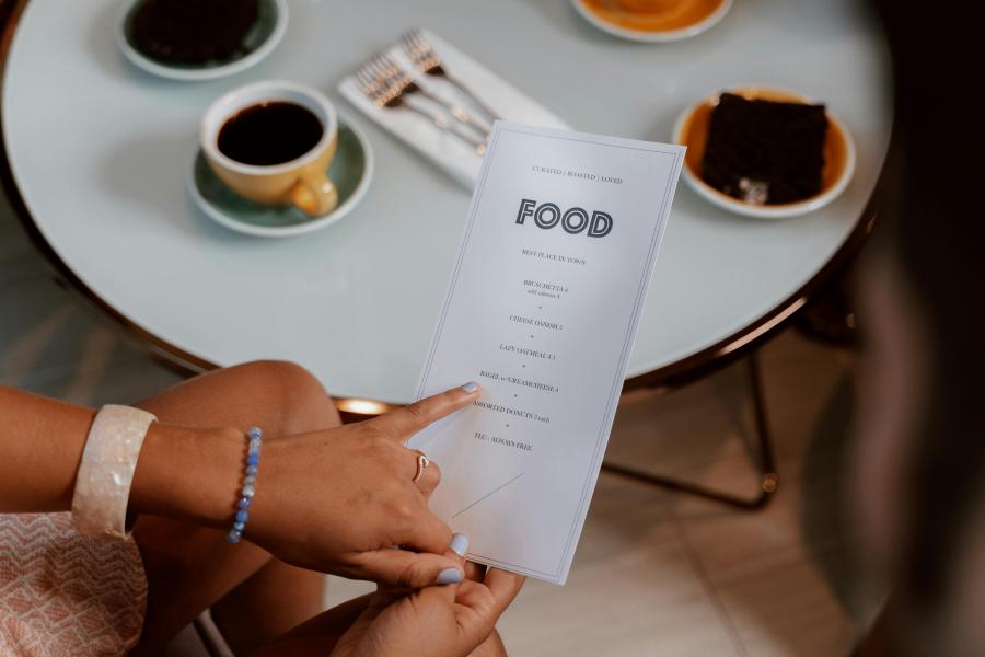 Food menu with someone pointing to items, restaurant table with coffee in the background