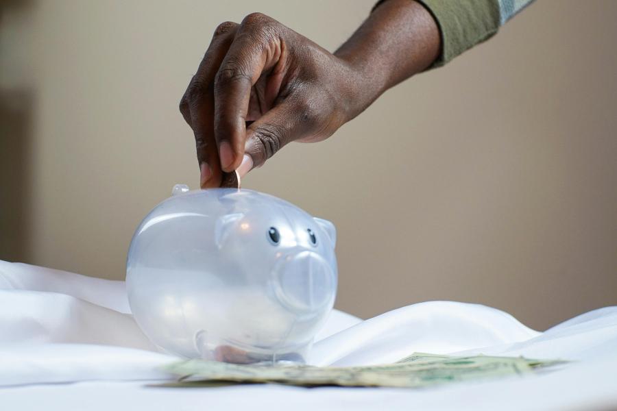A hand putting coins into a transparent plastic piggy bank