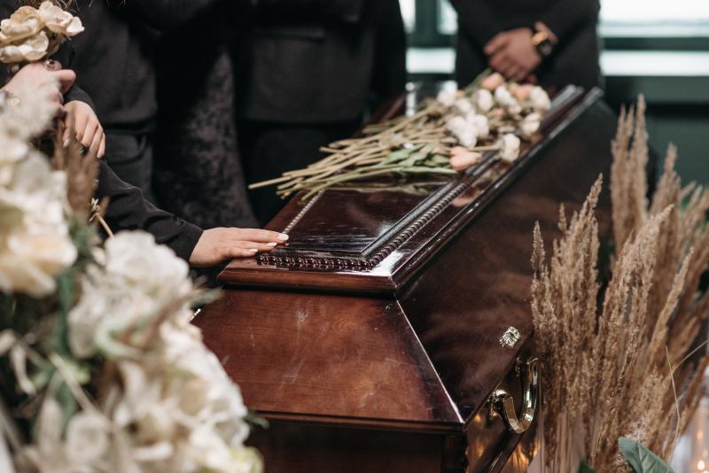 Hand touching wooden coffin with flowers on top of it