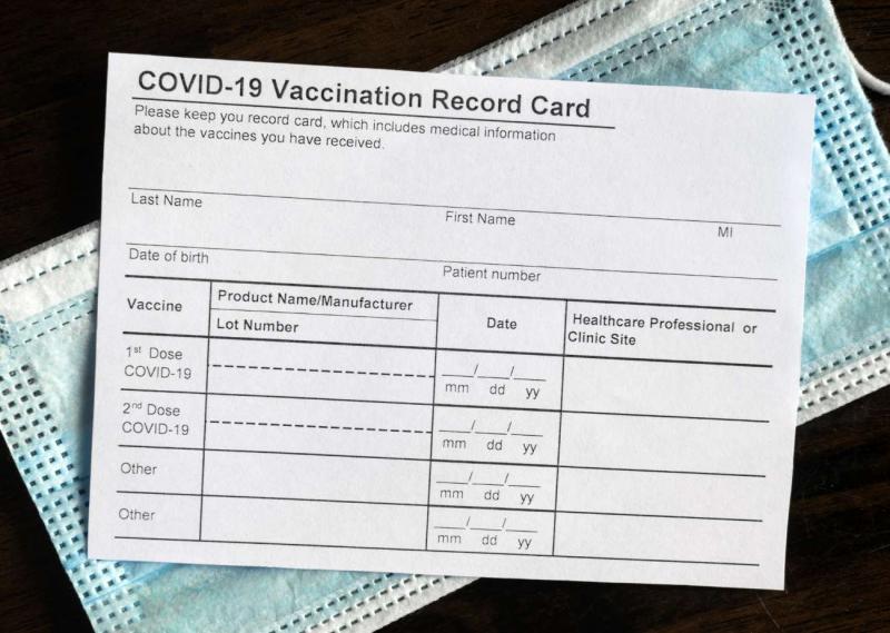A COVID-19 Vaccination record card on top of a blue and white disposable face mask