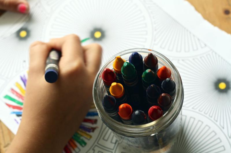 Close up of jar of crayons and a child's hand coloring an abstract design