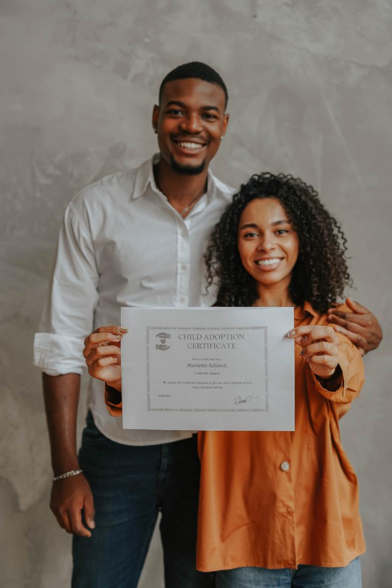 An African American couple smiling holding up a sign of an adoption certificate 