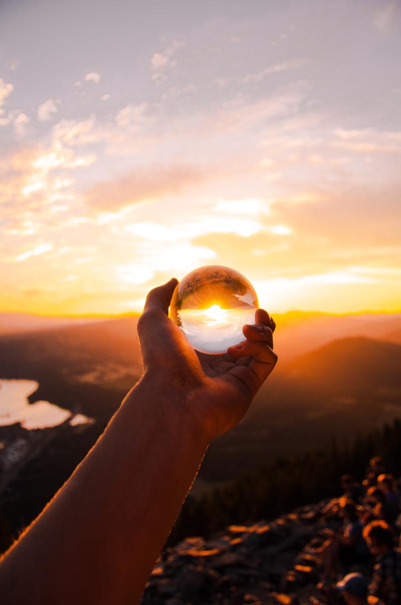 Hand holding a glass orb in front of a sunrise