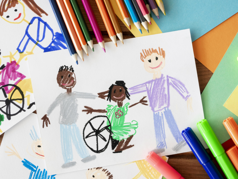 A coloring of a girl in a wheelchair with a boy to her left and right. The picture is surrounded with bright coloring pencils and paper