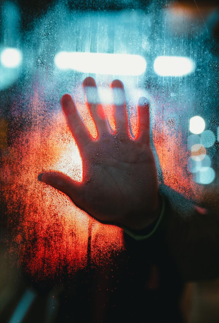 Hand on foggy glass with streetlights reflecting