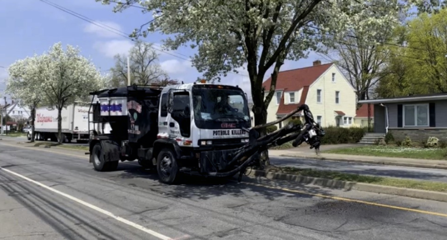 A "pothole killer" work truck clears a pothole on the side of a suburban road