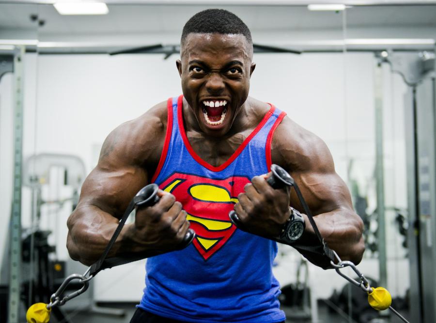 Man with muscles wearing superman tank top yelling intensely while exercising