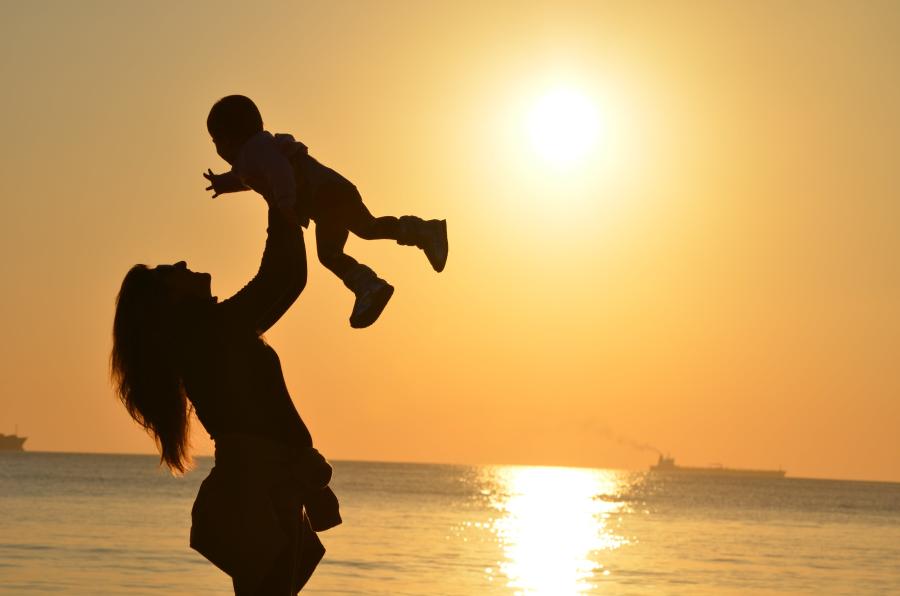 A silhouette of a mother lifting a child with a sunset over the ocean in the background